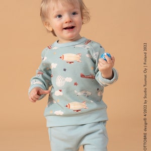 May include: A light blue toddler sweatshirt with a print of aeroplanes, hot air balloons, and stars. The sweatshirt has a crew neck and long sleeves.