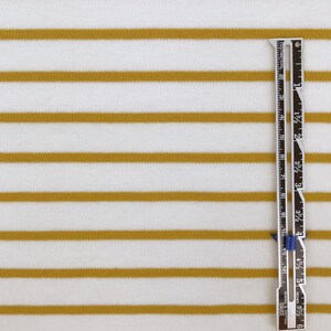 May include: White fabric with thin, horizontal, mustard yellow stripes. A ruler is placed vertically on the right side of the fabric. The ruler is marked in inches and centimeters.