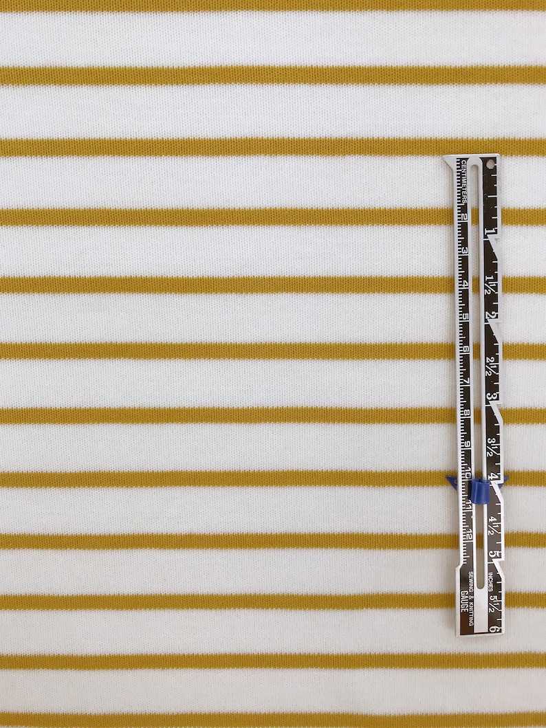 May include: White fabric with thin, horizontal, mustard yellow stripes. A ruler is placed vertically on the right side of the fabric. The ruler is marked in inches and centimeters.