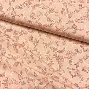May include: A close-up of a soft, peach-coloured fabric with a repeating pattern of abstract shapes made of tiny brown dots. The fabric has a subtle sheen and a smooth texture.