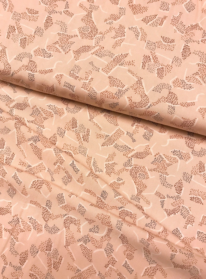 May include: A close-up of a soft, peach-coloured fabric with a repeating pattern of abstract shapes made of tiny brown dots. The fabric has a subtle sheen and a smooth texture.