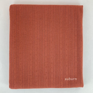 Peut inclure: Un gros plan sur un tissu couleur rouille avec un motif textur&eacute; et c&ocirc;tel&eacute;. Le tissu a un l&eacute;ger brillant et est doux au toucher. Le mot "auburn" est imprim&eacute; en blanc dans le coin inf&eacute;rieur droit.