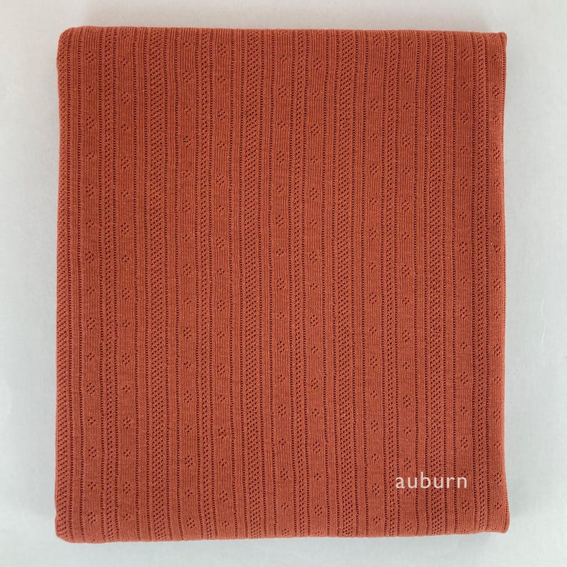 Peut inclure: Un gros plan sur un tissu couleur rouille avec un motif textur&eacute; et c&ocirc;tel&eacute;. Le tissu a un l&eacute;ger brillant et est doux au toucher. Le mot "auburn" est imprim&eacute; en blanc dans le coin inf&eacute;rieur droit.