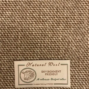Puede incluir: Un primer plano de una tela tejida marr&oacute;n y blanca con una etiqueta que dice "Natural Wool - Environment Friendly - No colorants - Undyed colour - European Fabric by FITECOM".