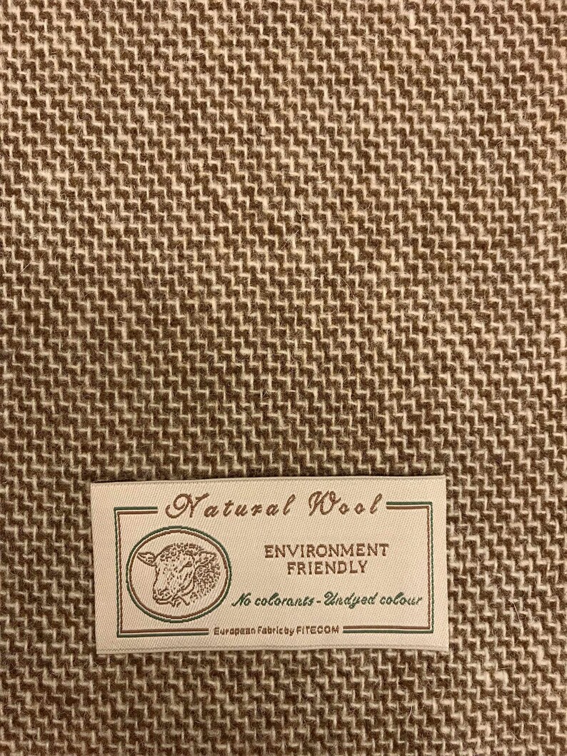 Puede incluir: Un primer plano de una tela tejida marr&oacute;n y blanca con una etiqueta que dice "Natural Wool - Environment Friendly - No colorants - Undyed colour - European Fabric by FITECOM".