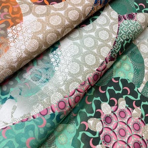 May include: A fabric with a patchwork design featuring various geometric patterns in shades of green, brown, pink, and white. The fabric has a subtle sheen and a soft texture.