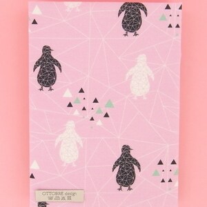 May include: Pink fabric featuring a geometric design of penguins in black and white, with small triangles in black, white, and green. The fabric has a label that reads "OTTOBRE design". A ruler is at the bottom.