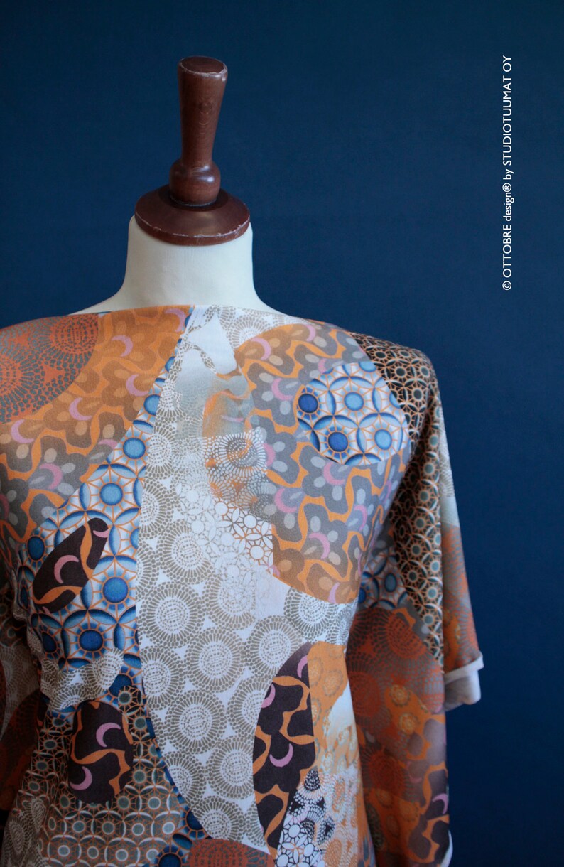 May include: A white, orange, brown, and blue patterned fabric with a geometric design. The fabric is draped over a dress form.