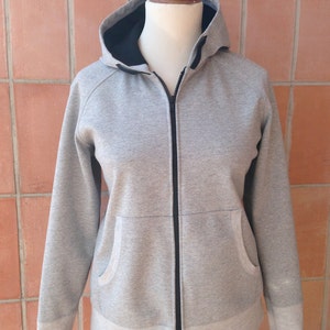 Puede incluir: Una sudadera con capucha gris con cremallera negra y forro de capucha negro. La sudadera tiene un bolsillo a cada lado y un dobladillo de canal&eacute;.