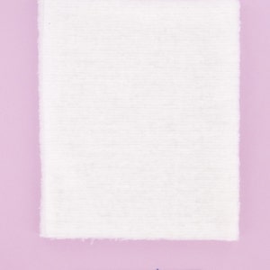Puede incluir: Un trozo de tela blanco rectangular con una textura ligeramente rugosa. La tela est&aacute; tendida sobre una superficie rosa claro.