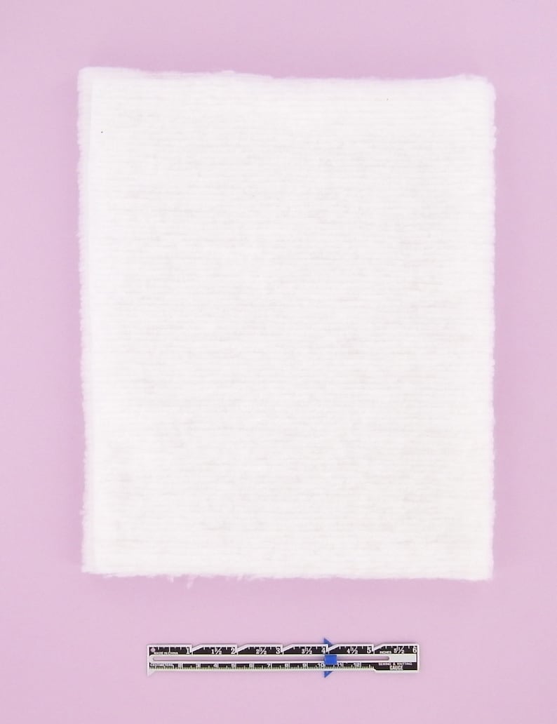 Puede incluir: Un trozo de tela blanco rectangular con una textura ligeramente rugosa. La tela est&aacute; tendida sobre una superficie rosa claro.
