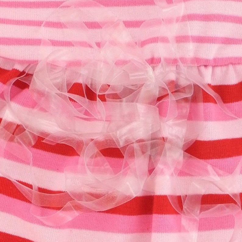 May include: Close-up of a striped fabric in shades of pink and red, with a delicate, sheer, light pink ribbon embellishment. The fabric has horizontal stripes of varying widths and colors.