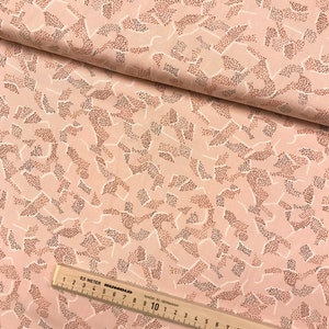 May include: Pink fabric with a white and brown abstract pattern. The pattern is made up of small dots and lines. The fabric is folded in half and a ruler is visible in the bottom right corner.
