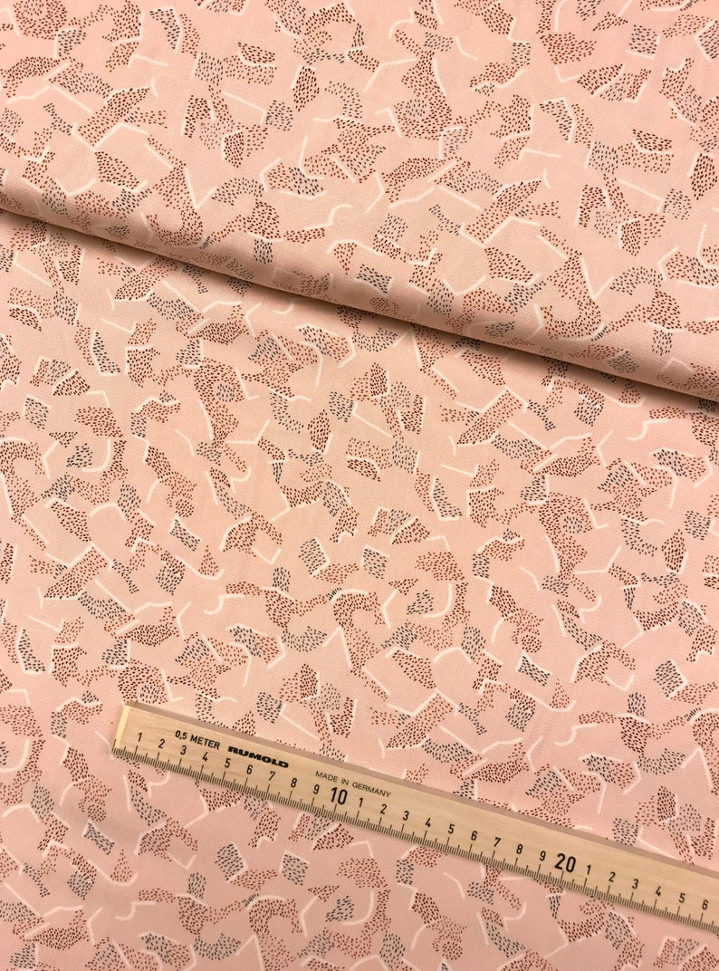 May include: Pink fabric with a white and brown abstract pattern. The pattern is made up of small dots and lines. The fabric is folded in half and a ruler is visible in the bottom right corner.
