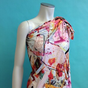 May include: One-shoulder dress with a colorful abstract print featuring musical notes, letters, and splashes of color. The dress is made of a soft, flowing fabric.