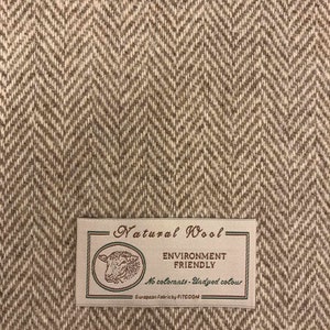 Puede incluir: Un primer plano de una tela de espiga marr&oacute;n y blanca con una etiqueta que dice "Natural Wool - Environment Friendly - No colorants - Undyed colour - European Fabrics by FITECOM".