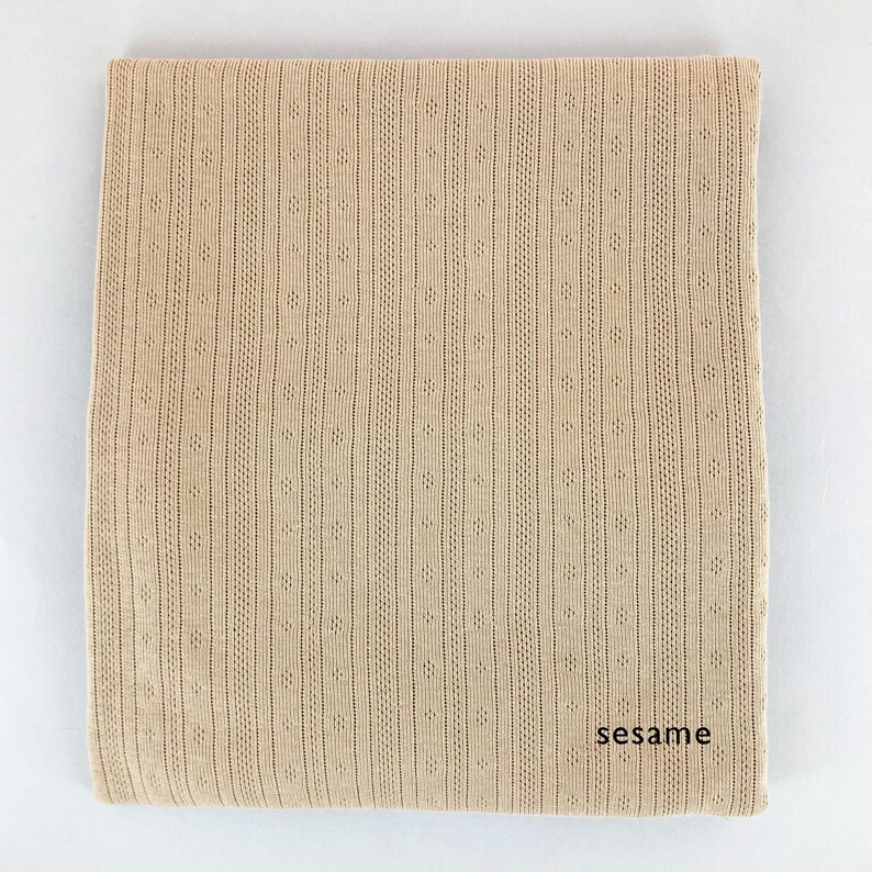 Peut inclure: Un tissu tricot&eacute; beige avec un motif textur&eacute;. Le tissu a un l&eacute;ger brillant et une sensation douce et fluide. Le tissu est &eacute;tiquet&eacute; "sesame".