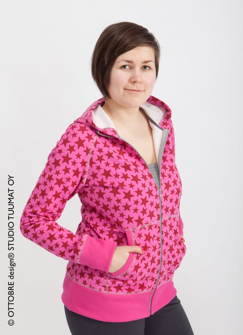 Puede incluir: Una sudadera con capucha rosa con un estampado de estrellas rojas. La sudadera tiene una cremallera y dos bolsillos.