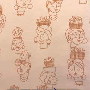 May include: A pink fabric with a repeating pattern of brown line drawings of women's faces with various head coverings and baskets of fish. The fabric has a subtle texture.
