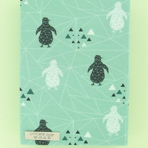 May include: A rectangular fabric piece with a light teal background featuring a geometric pattern of white lines, black and white penguins, and triangles. A small label reads "OTTOBRE design". A ruler is at the bottom.