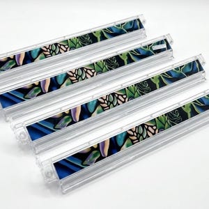 May include: Four clear plastic organizers with a colorful floral design. The design features blue, green, and purple leaves and flowers on a black background. The organizers are rectangular and have a clear, ridged design.