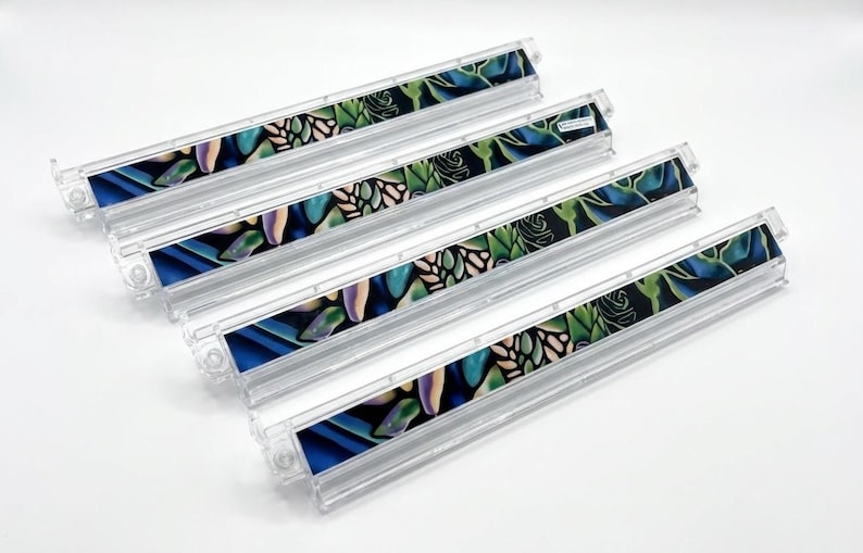 May include: Four clear plastic organizers with a colorful floral design. The design features blue, green, and purple leaves and flowers on a black background. The organizers are rectangular and have a clear, ridged design.