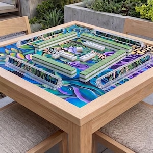 May include: A wooden Mahjong table with a colorful floral design on the playing surface. Green and white tiles are arranged on the table, along with clear tile racks. The table is surrounded by wooden chairs.