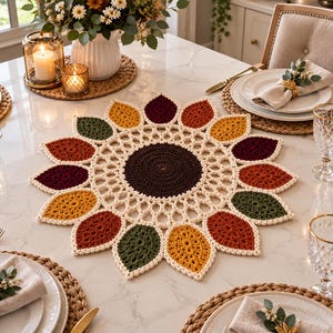Pode incluir: Um lugar americano redondo em crochê com um centro castanho escuro rodeado por um anel de rede creme e uma borda externa de motivos em forma de pétalas em tons alternados de amarelo mostarda, vermelho escuro, laranja e verde floresta.