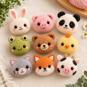 May include: A collection of nine round, crocheted animal heads including a rabbit, pig, panda, frog, bear, chick, cat, fox, and cow. Each plush figure features black bead eyes, embroidered facial details, and soft, textured yarn construction.