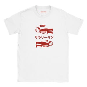 May include: A white short-sleeved t-shirt featuring a red graphic of two figures in suits floating horizontally. The top figure has a speech bubble saying "LET'S FLY" and the bottom figure has one saying "OK". The Japanese text "サラリーマン" is centered between them.