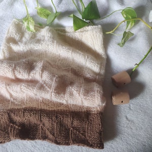 May include: A knitted scarf with a gradient of white, cream, and brown. The scarf is made with a textured stitch pattern.