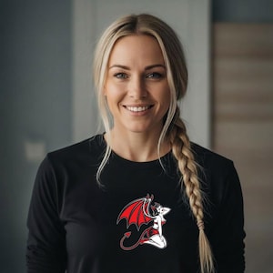 May include: Black long-sleeve shirt featuring a red and white devil graphic. The graphic depicts a woman with red wings, a tail, and a devil horn. The woman in the image is smiling and has blonde hair.