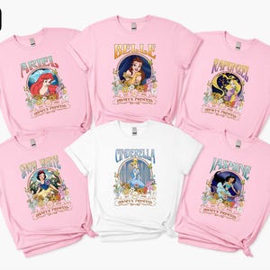 a collection of pink t-shirts featuring Disney princess characters, including Belle, Rapunzel, Snow White, Cinderella, and Jasmine.