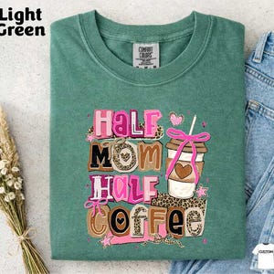 A green t-shirt with a colorful graphic design that says "Half Mom Half Coffee" and features a coffee cup and other decorative elements.