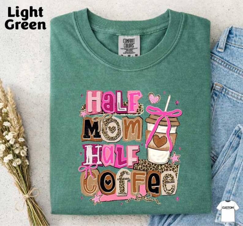 A green t-shirt with a colorful graphic design that says "Half Mom Half Coffee" and features a coffee cup and other decorative elements.