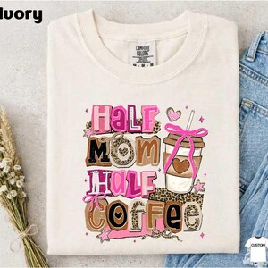 A white t-shirt with a colorful graphic design that says "Half Mom Half Coffee" along with a coffee cup and other decorative elements.