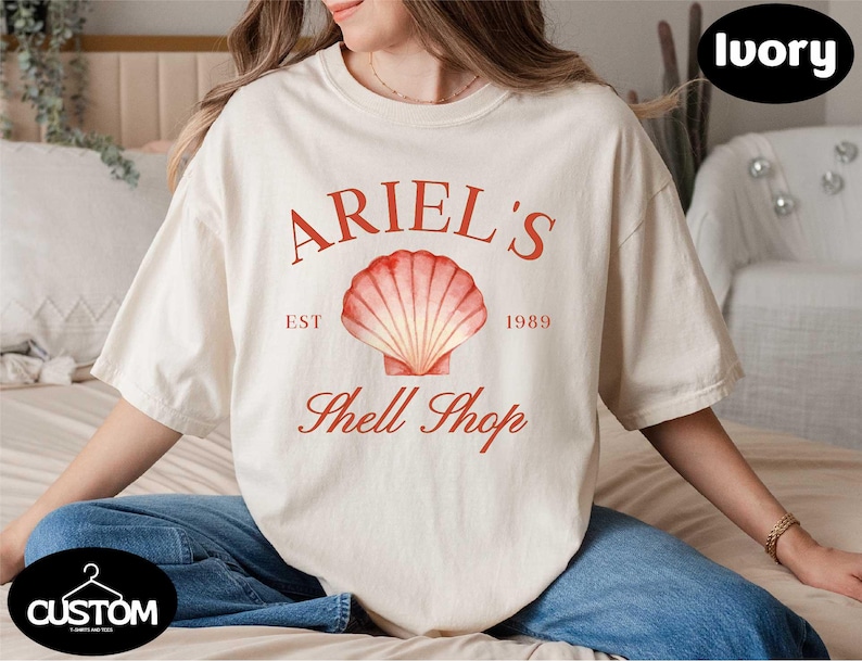 a woman sitting on a bed wearing a t - shirt that says ariel's