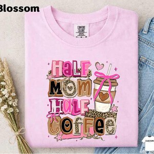 A pink t-shirt with a graphic design featuring the text "Half Mom Half Coffee" and a coffee cup with a heart-shaped ribbon.