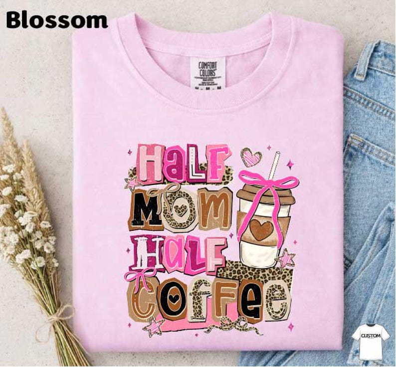 A pink t-shirt with a graphic design featuring the text "Half Mom Half Coffee" and a coffee cup with a heart-shaped ribbon.