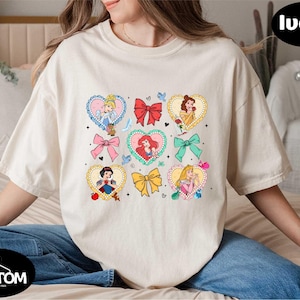 a woman sitting on a bed wearing a t - shirt with princesses on it