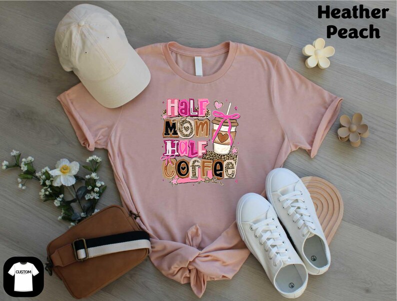 a pink t-shirt with a graphic design, a white baseball cap, a brown purse, a pair of white sneakers, and some flowers on a wooden surface.