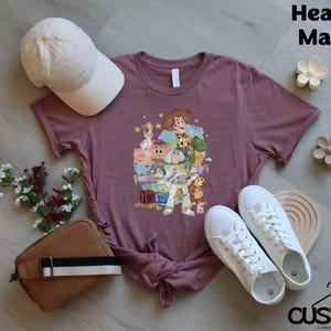 a purple t-shirt with a character design, a white baseball cap, a brown purse, a pair of white sneakers, and some flowers on a wooden surface.