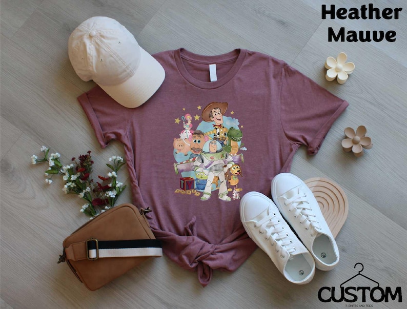 a purple t-shirt with a character design, a white baseball cap, a brown purse, a pair of white sneakers, and some flowers on a wooden surface.