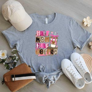 a gray t-shirt with a graphic design, a white baseball cap, a brown purse, a pair of white sneakers, and some flowers on a wooden surface.