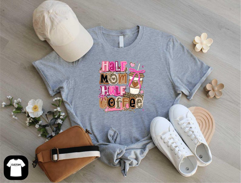 a gray t-shirt with a graphic design, a white baseball cap, a brown purse, a pair of white sneakers, and some flowers on a wooden surface.