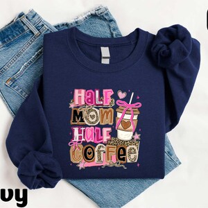 A navy blue sweatshirt with a colorful graphic design that says "Half Mom Half Coffee" printed on it, along with a coffee cup and other coffee-related items.