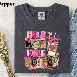 A gray t-shirt with a colorful graphic design that says "Half Mom Half Coffee" and features a coffee cup and other decorative elements.