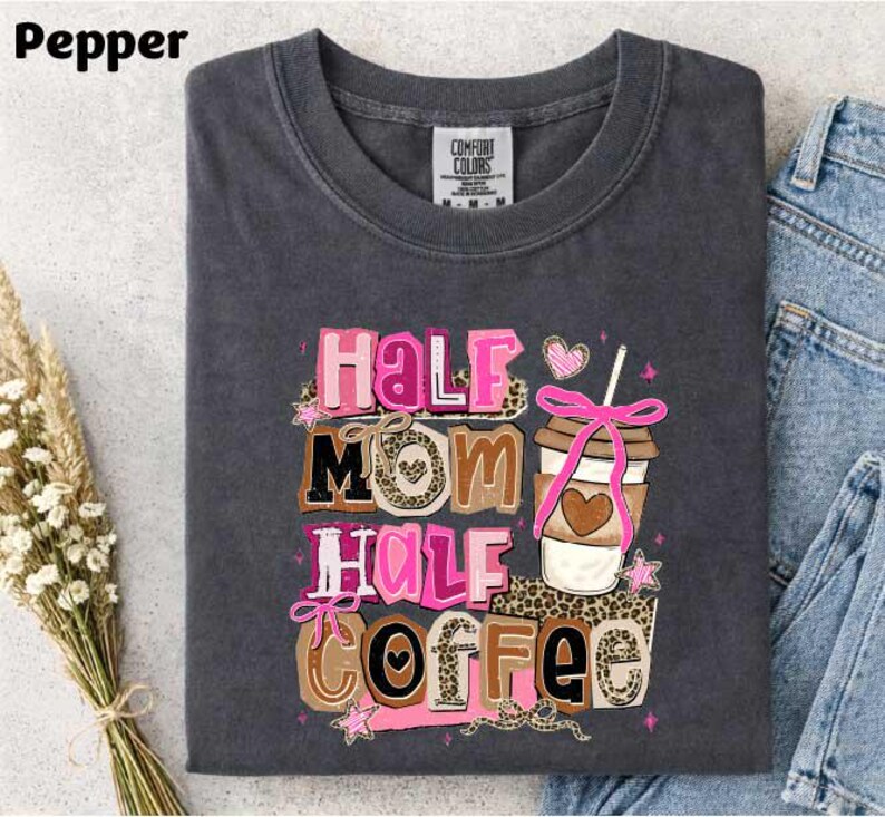 A gray t-shirt with a colorful graphic design that says "Half Mom Half Coffee" and features a coffee cup and other decorative elements.