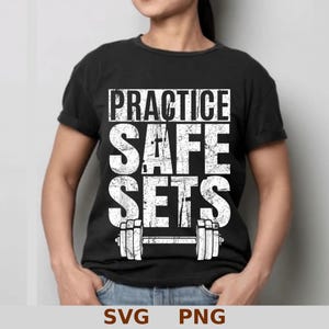 Könnte beinhalten: Schwarzes T-Shirt mit dem Text "PRACTICE SAFE SETS" in verblichener weißer Schrift und einer Hantel-Grafik. Die Person trägt eine blaue Jeans.