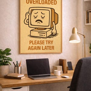 Può includere: Un poster incorniciato con un'illustrazione di computer vintage e il testo "SYSTEM OVERLOADED PLEASE TRY AGAIN LATER". Il poster è su una scrivania con un laptop, una tazza di caffè e forniture per ufficio.